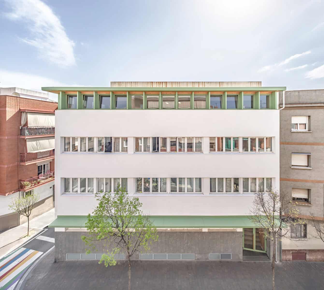 Fachada principal de la Escuela Santa Eulàlia de Cornellà rehabilitada por Taller SAU con sistema SATE, nueva remonta de madera y soportal verde RAL 6021