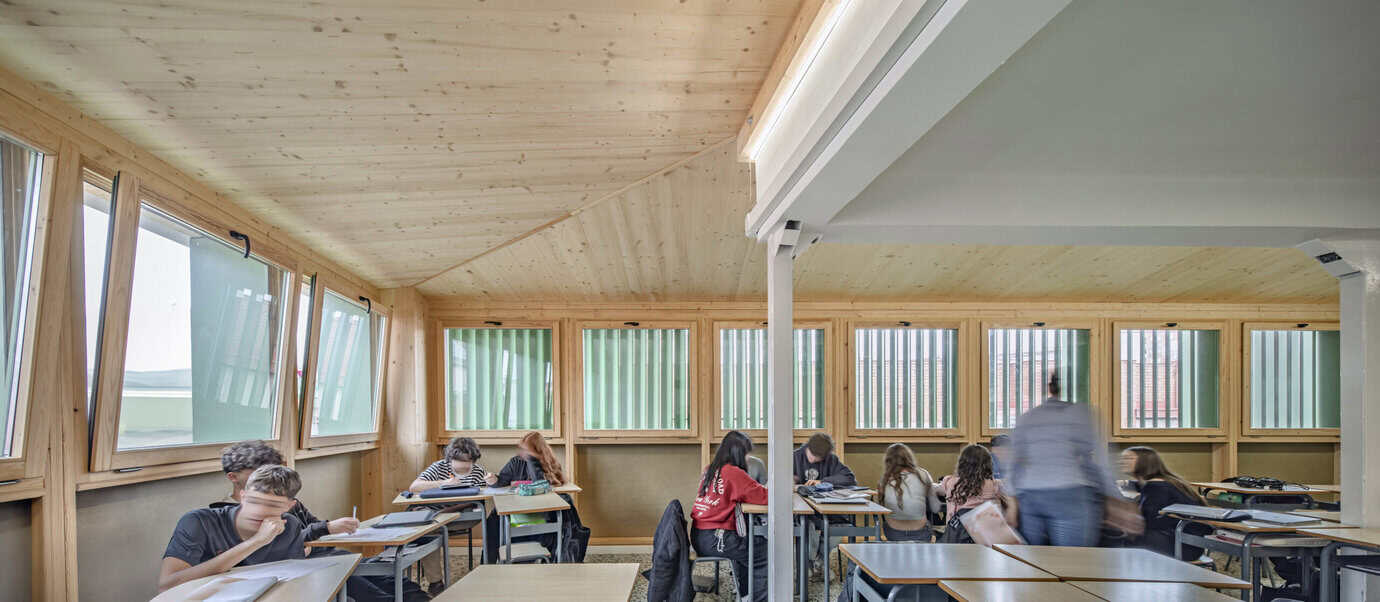 Aula de la Escuela Santa Eulàlia de Cornellà con alumnos, estructura de madera de abeto y lamas de control solar verdes, rehabilitación de Taller SAU