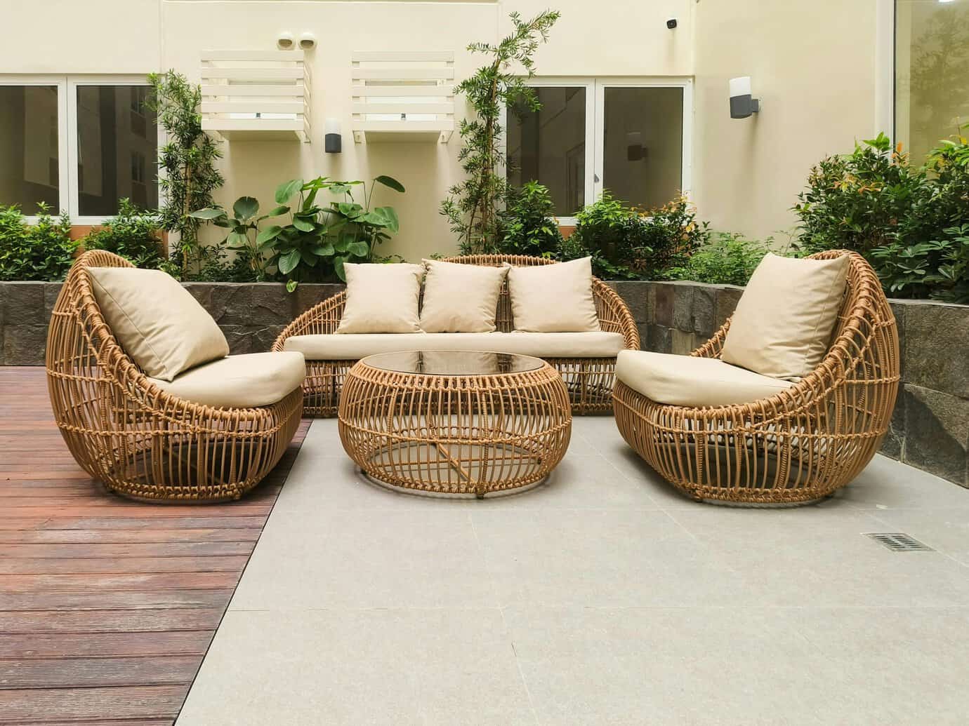 Terraza exterior con combinación de pavimento de gres porcelánico en tonos neutros y tarima de madera, con mobiliario de ratán y vegetación