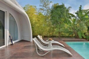 arima de madera WPC junto a piscina exterior con tumbonas de diseño y vegetación tropical