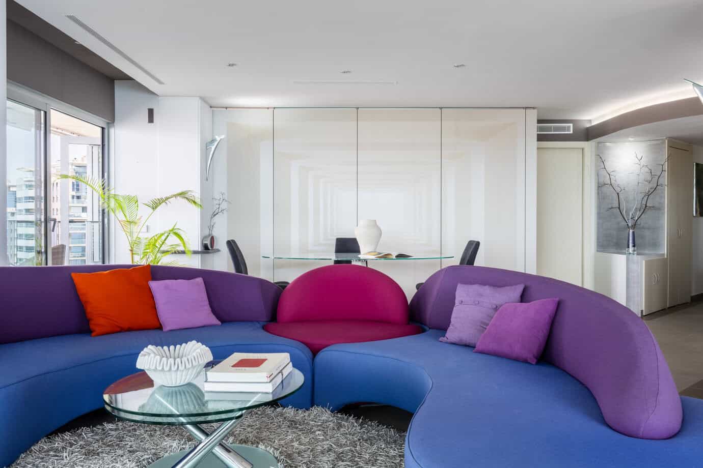 Salón principal con sofá modular Roche Bobois y panel móvil acabado mármol, que integra el acceso a la habitación de invitados